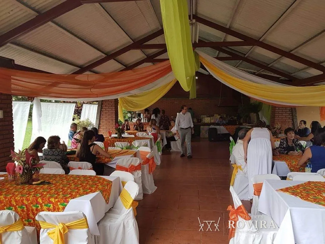 Techo de tela naranja y amarillo en salón rústico, mesas con mantel tropical naranja
