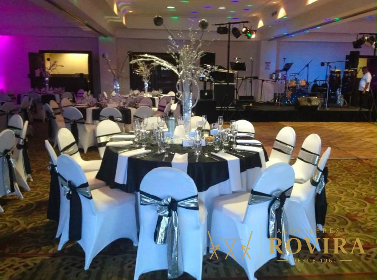 Salón con mesas redondas, forros de silla blancos y lazos negros y pista iluminada de fiesta