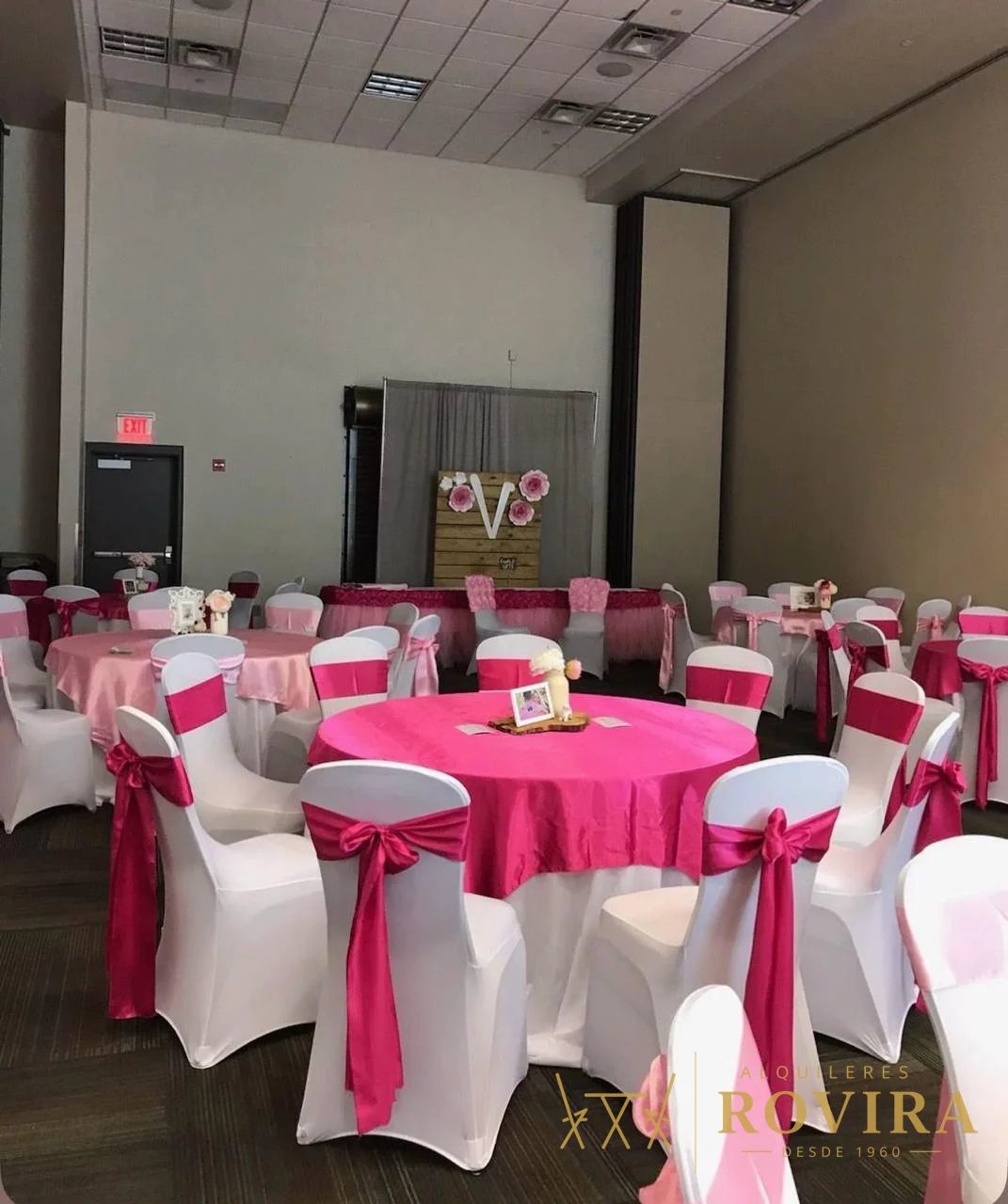 Mesas redondas con mantel fucsia y forros de silla blancos con lazo fucsia, salón de eventos