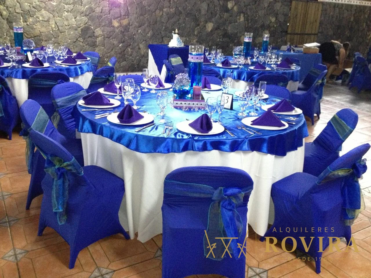 Mesa redonda vestida en azul rey con servilletas, cristalería y centro de mesa, montaje formal