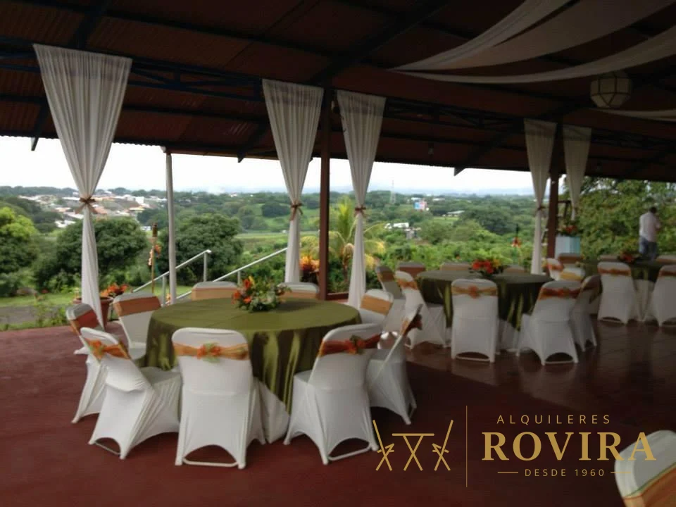 Terraza con mesas redondas en mantel verde olivo y forros de silla blancos, vista abierta