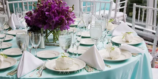 Mesa vestida con centro floral morado, cristalería y vajilla de evento