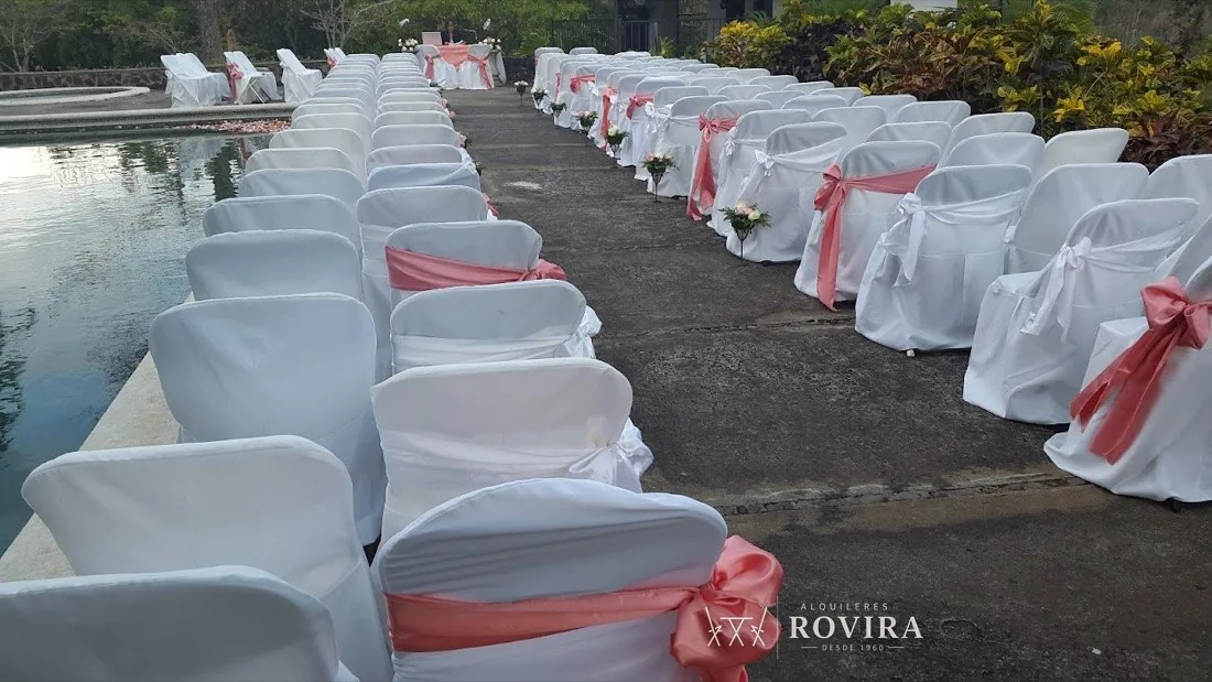 Boda junto a piscina al aire libre, sillas forradas blancas con lazo coral