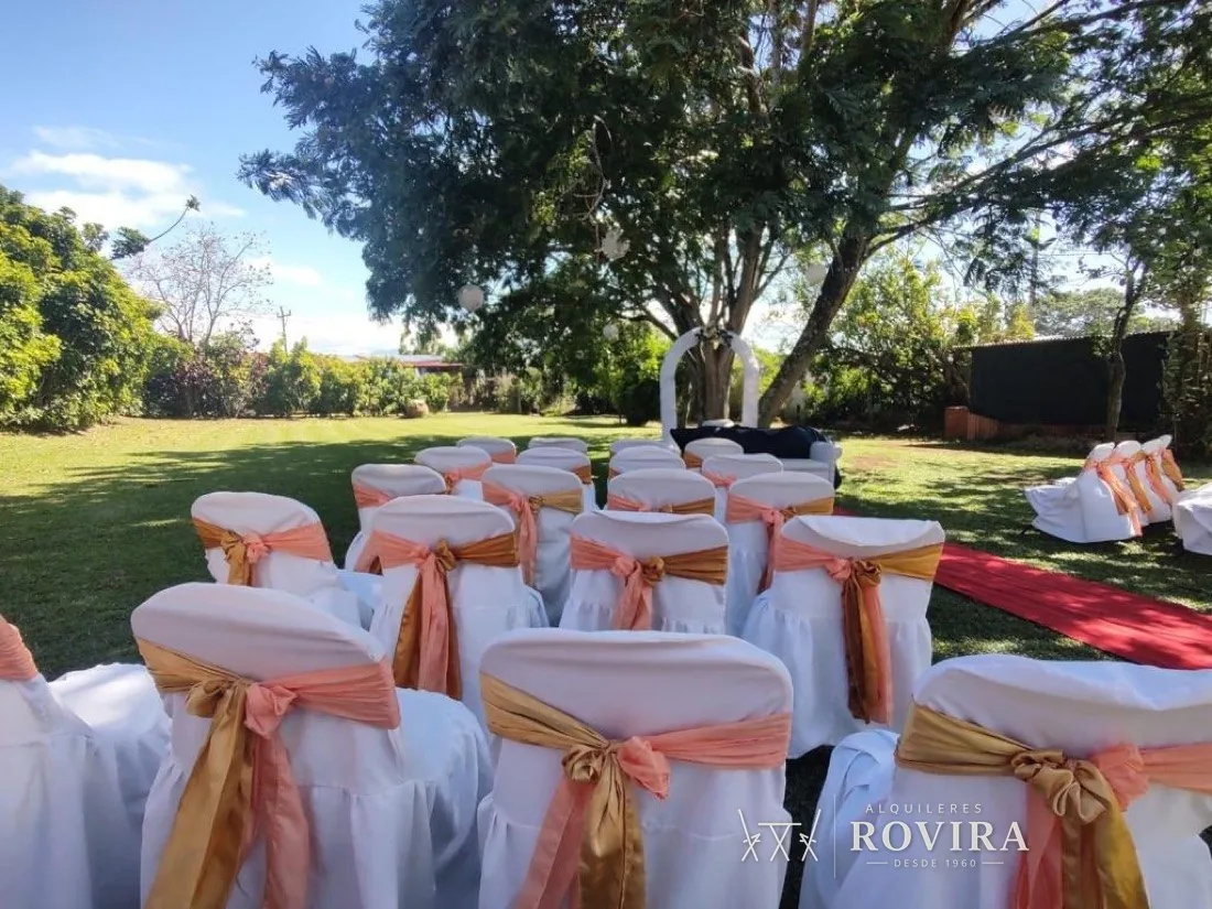 Ceremonia en jardín, sillas blancas con doble lazo coral y dorado, arco floral
