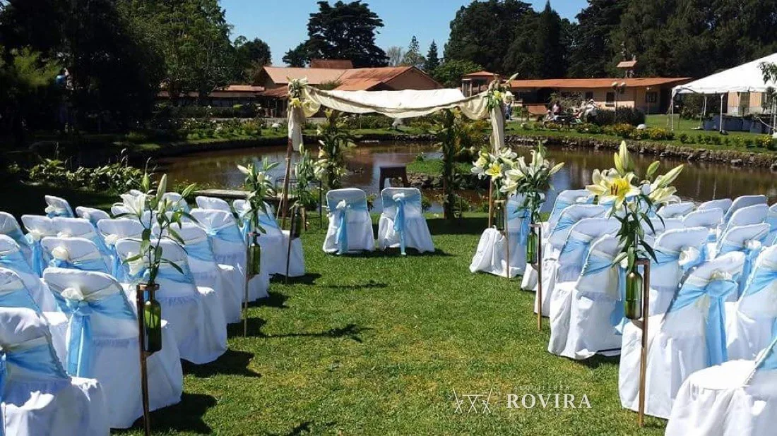 Ceremonia junto a laguna, sillas blancas con lazo celeste y arreglos de lirios