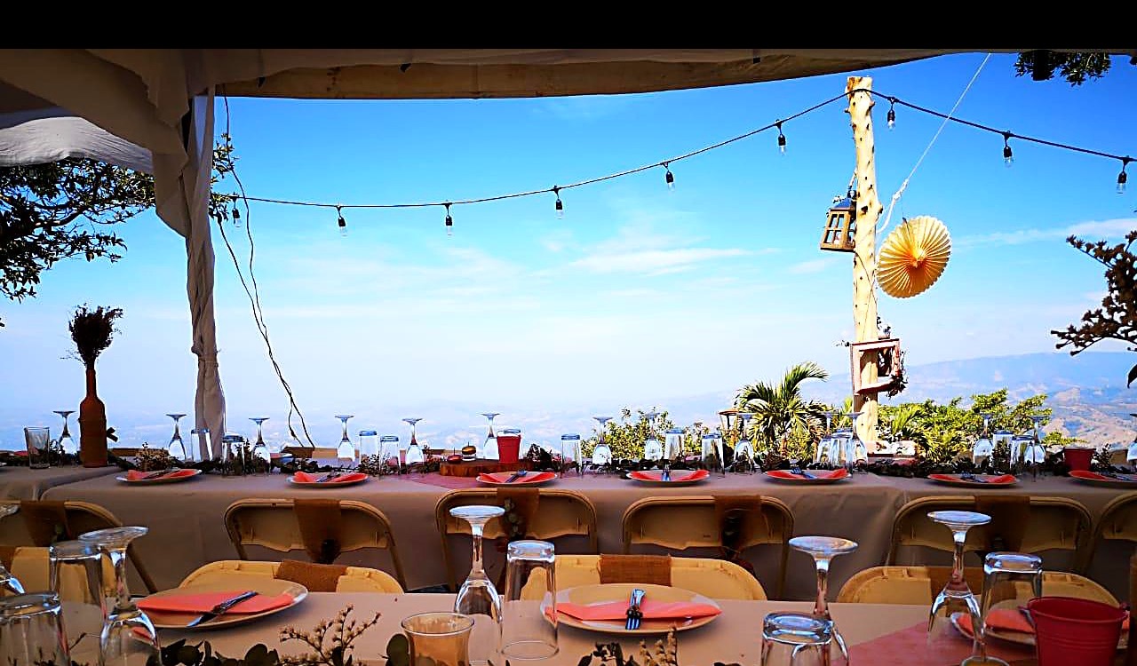 Silla plegable cromada con respaldar blanco y lazo café, mesa larga vestida sobre una montaña con vista panorámica