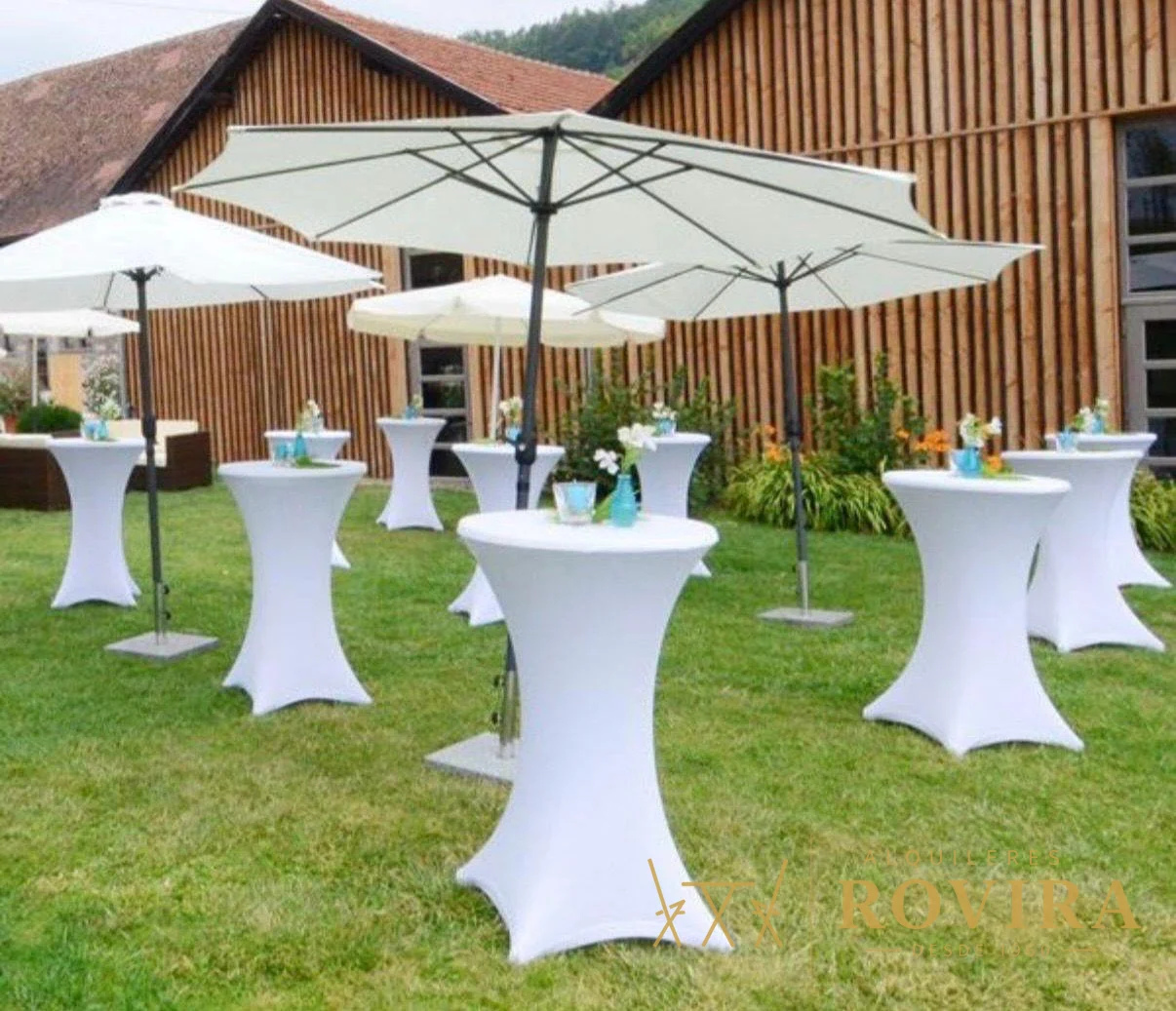 Varias mesas cocktaileras blancas con sombrillas en un jardín, montaje al aire libre