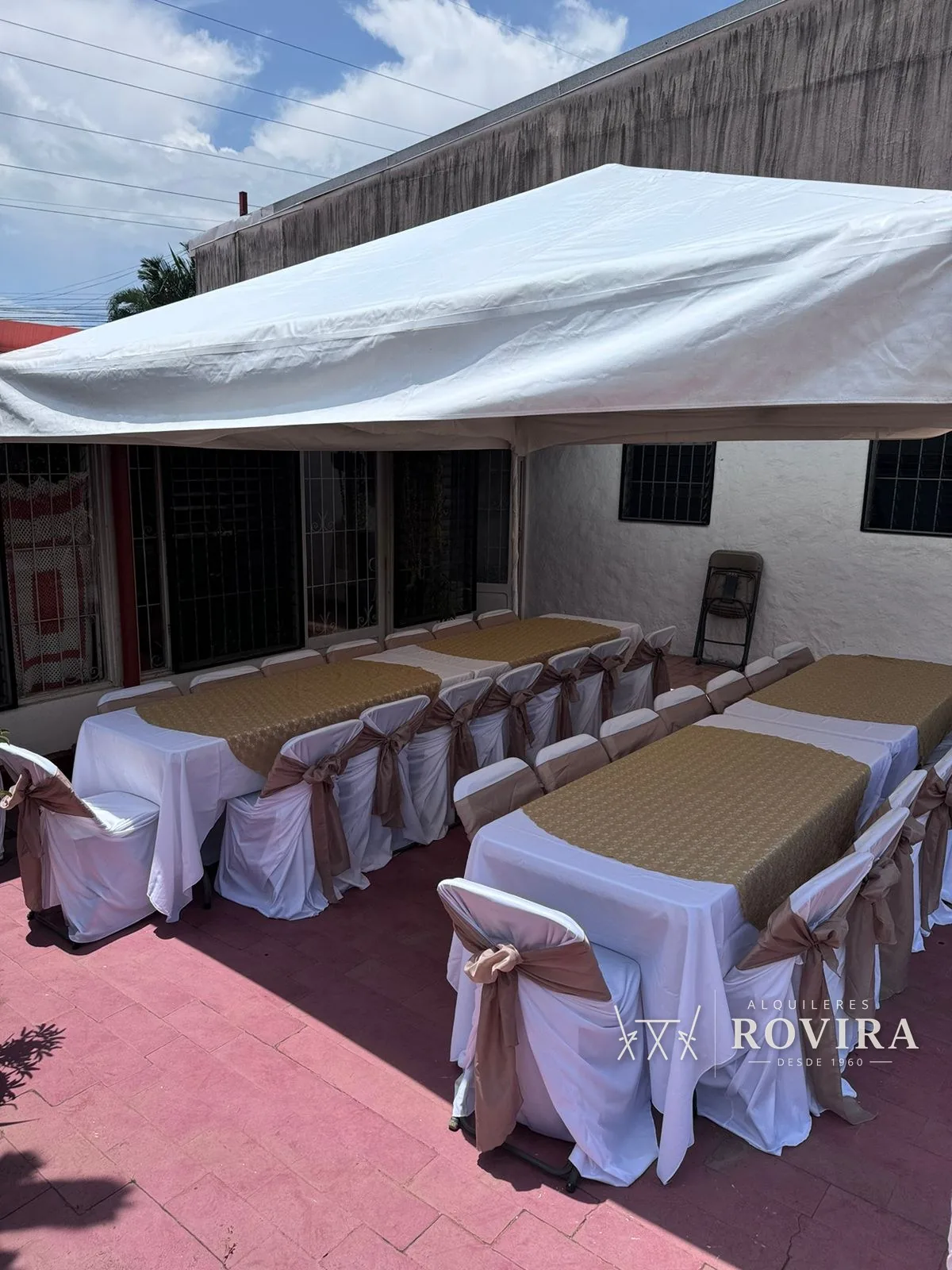 Toldo con mesas largas vestidas en blanco y café, terraza residencial