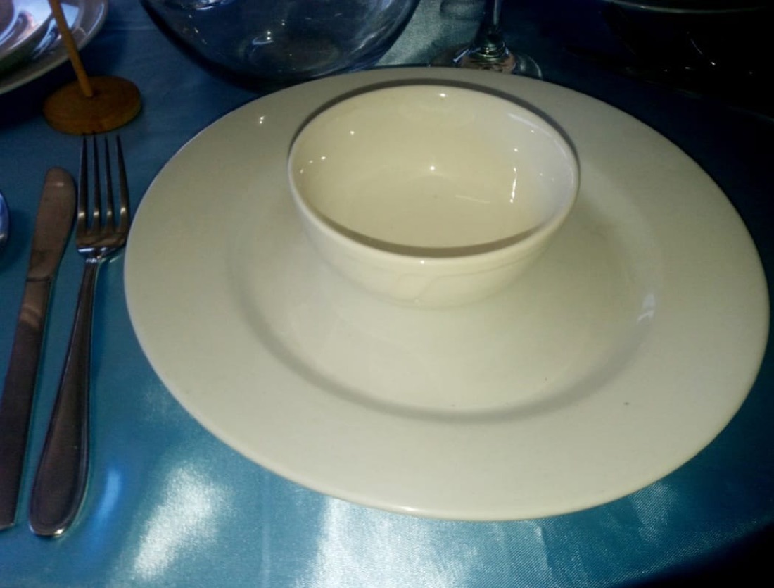 Plato blanco con bowl para sopa sobre mantel turquesa, con vela decorativa