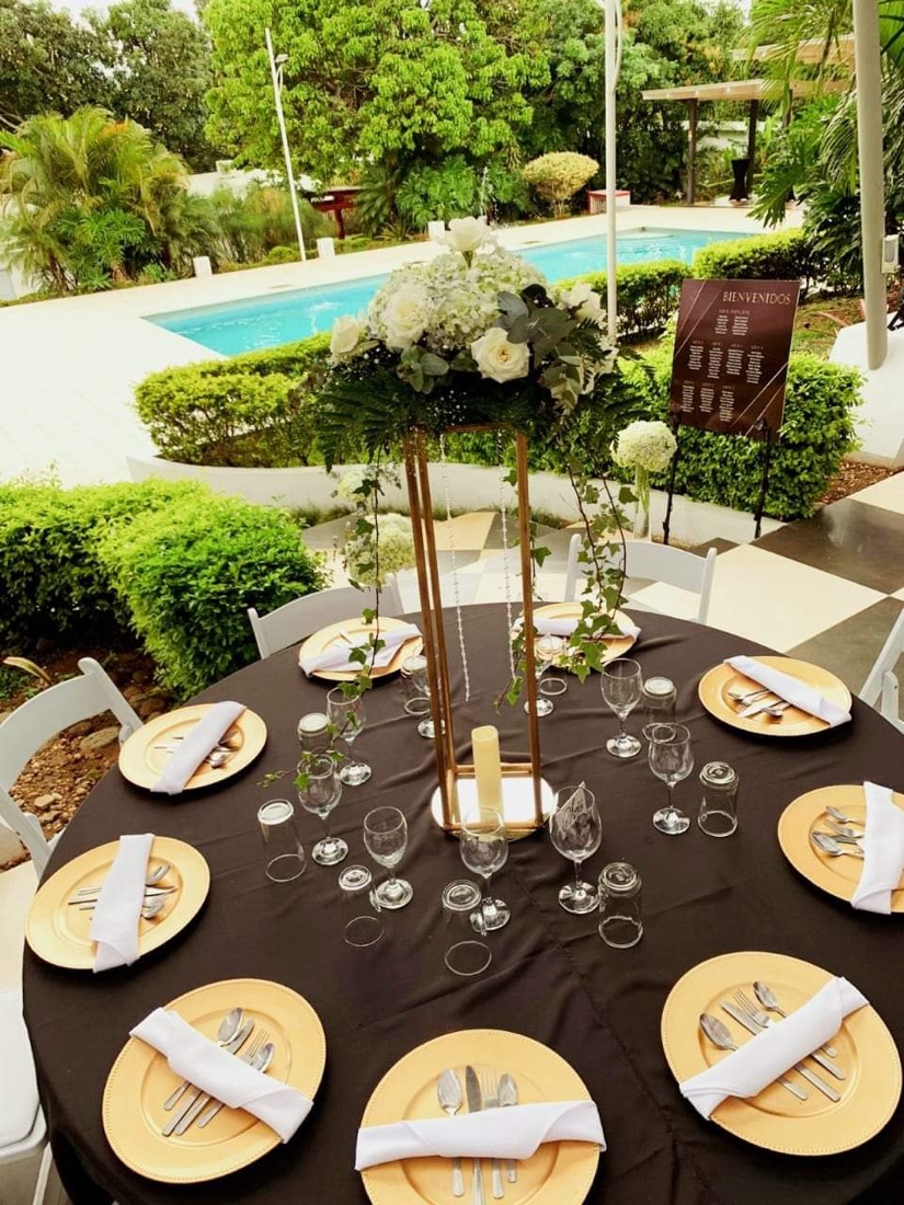 Mesa de boda al aire libre junto a piscina, platos base dorados, copas de vino y agua