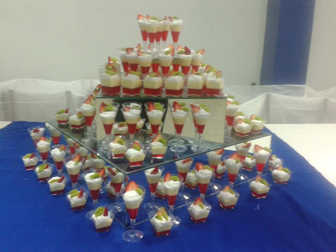 Mesa dulce con postres en vasitos y copas de vidrio sobre espejo