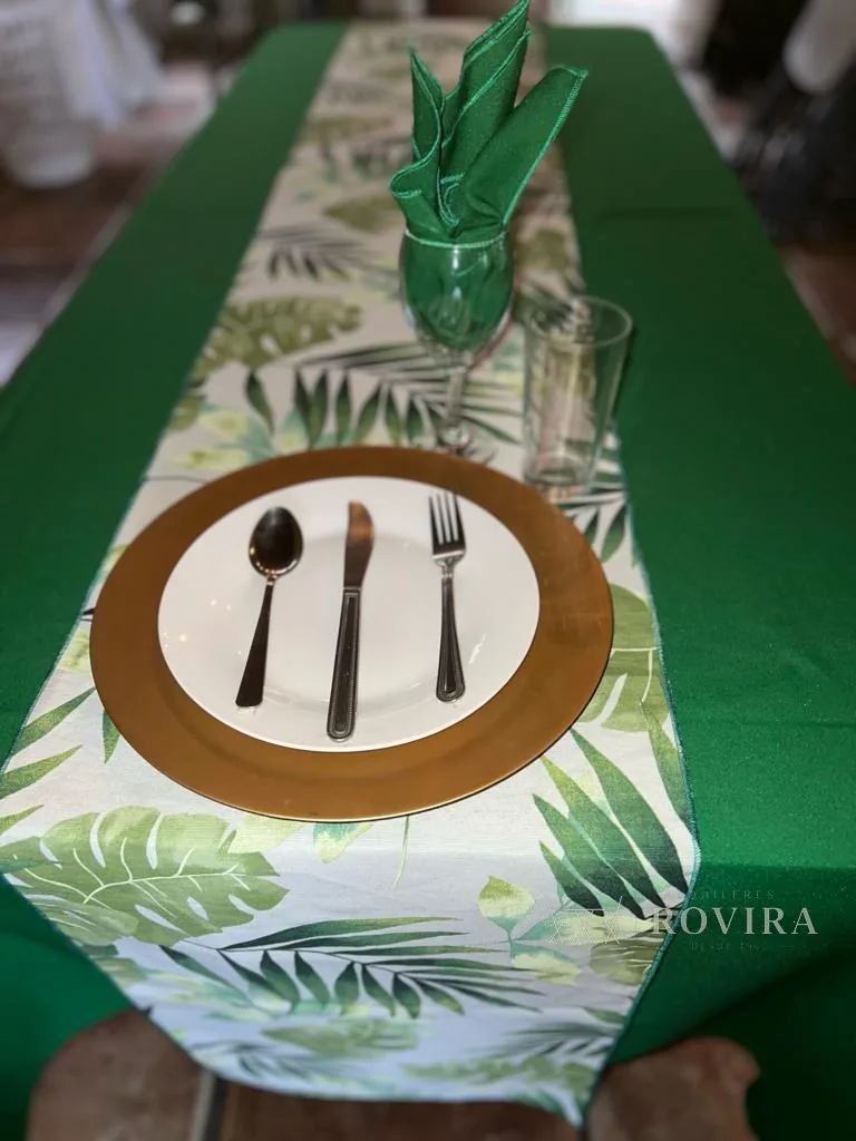 Puesto de mesa con camino tropical de hojas verdes, plato base dorado, servilleta verde y cubiertos