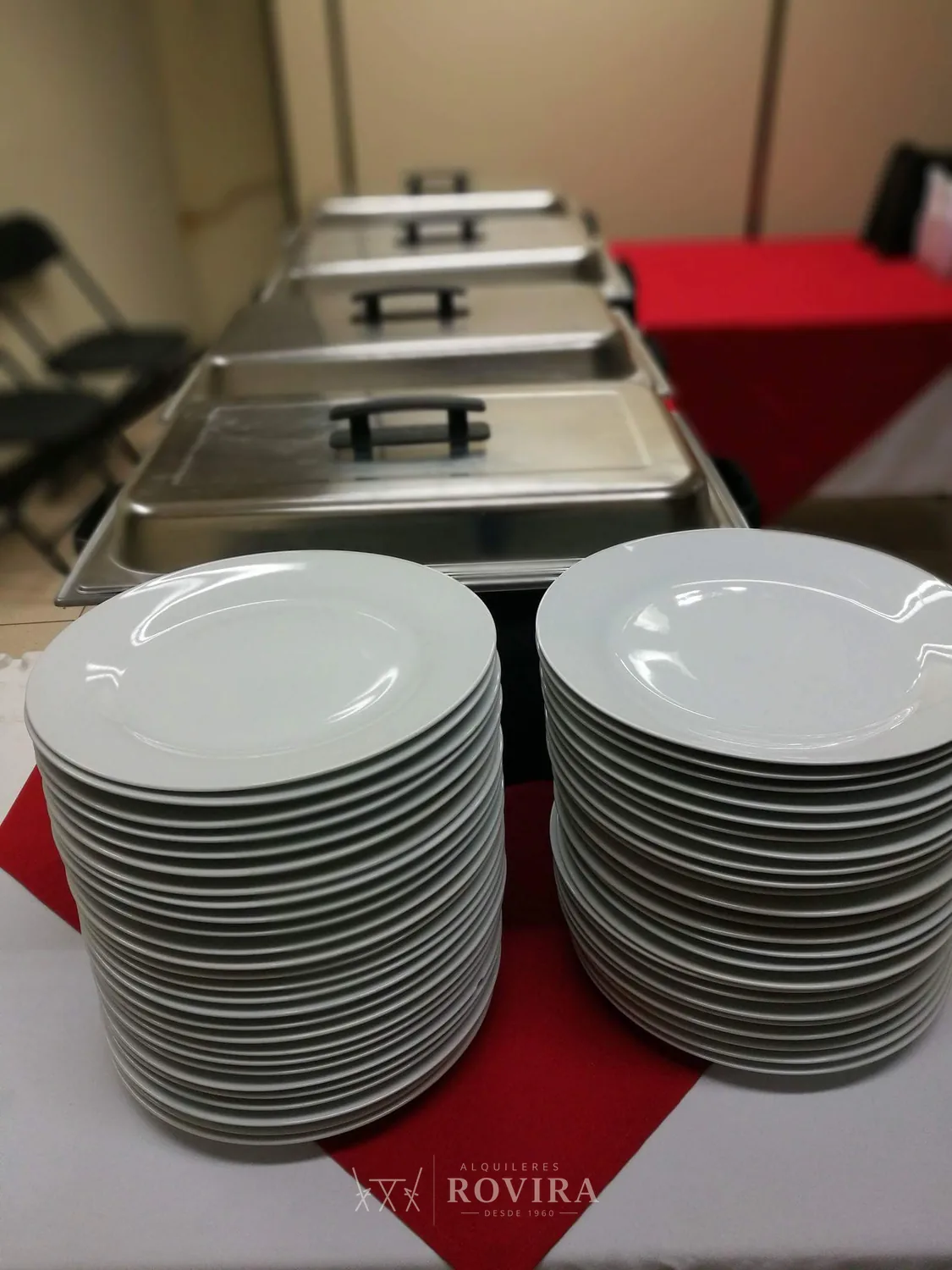 Buffet caliente con chafing dishes y platos apilados, servicio de catering