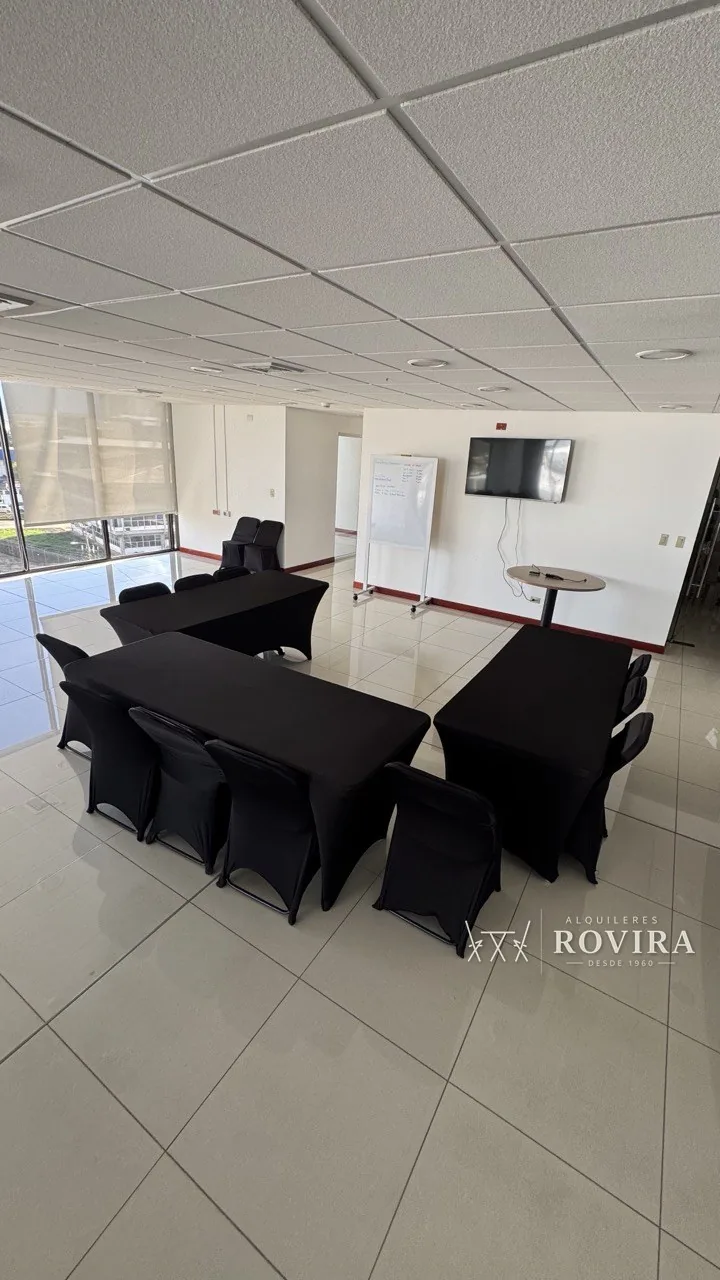Mesas rectangulares forradas en negro con sillas negras, montaje tipo capacitación en oficina