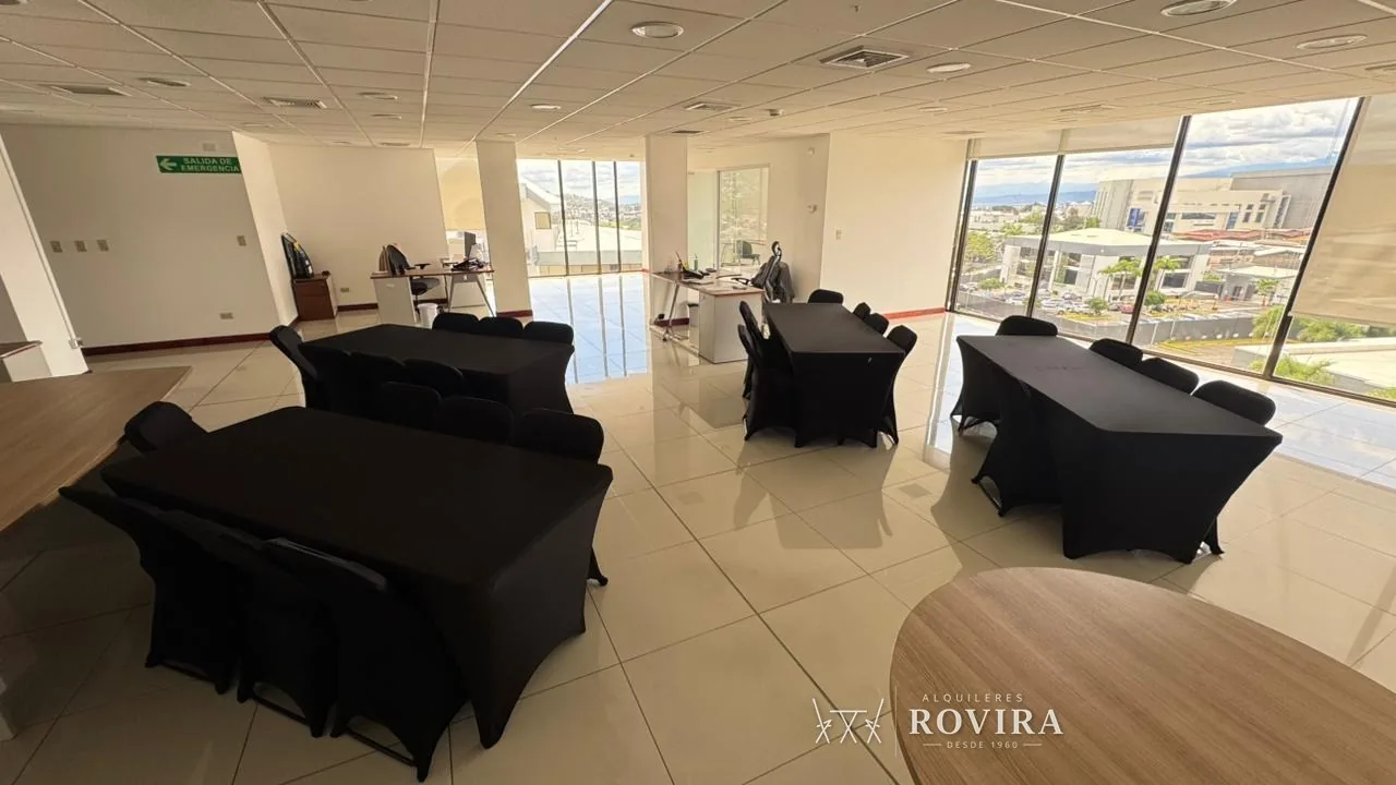 Mesas rectangulares negras dispuestas en oficina moderna con vista a la ciudad