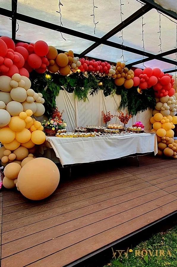 Arco de globos naranja y dorado con mesa de dulces