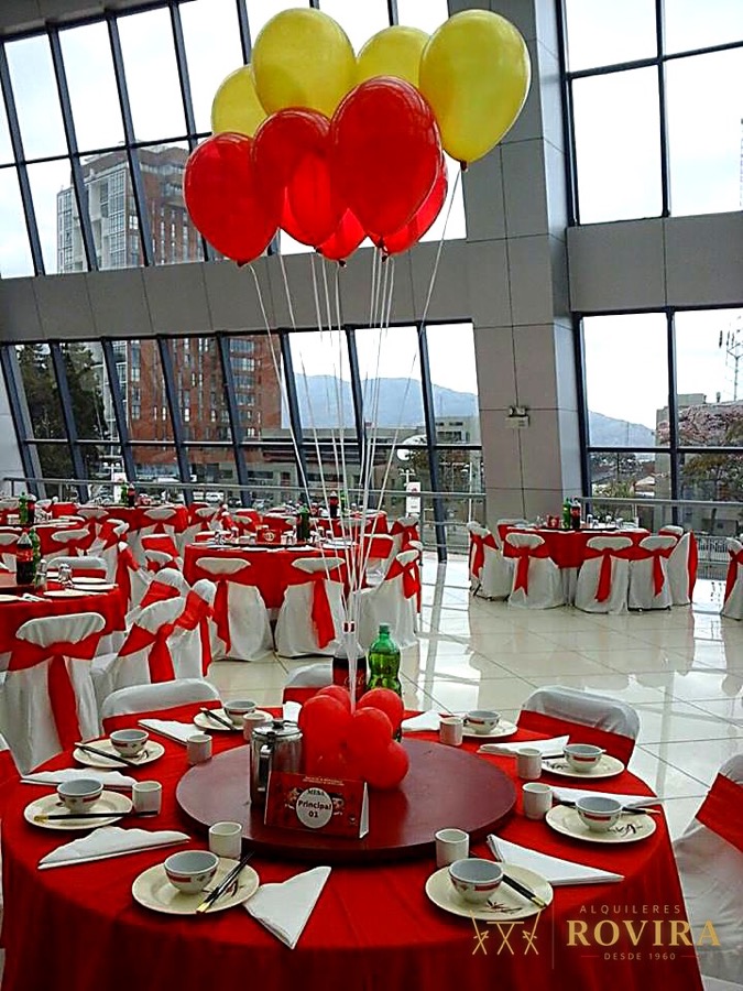 Evento corporativo en salón con vista a la ciudad, mesas rojas y blancas, globos rojos y amarillos