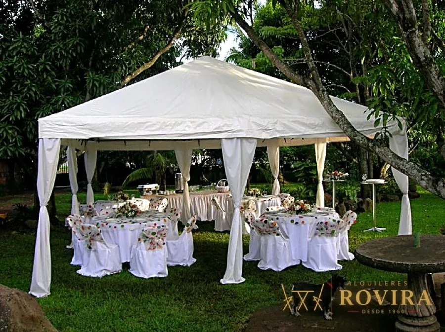Toldo blanco con mesas en jardín arbolado